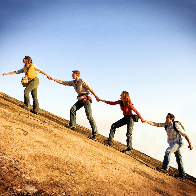 four adults holding hands while climbing a mountain.